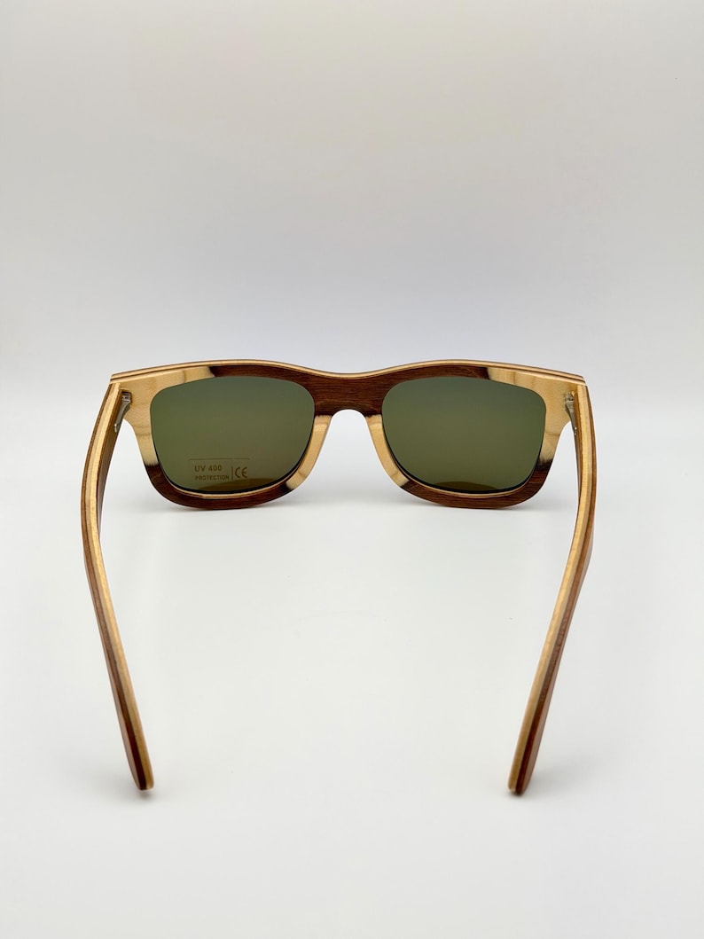 May include: Wooden-framed sunglasses with green lenses. The frames feature a combination of light and dark wood tones, creating a striped effect. The arms are a lighter wood color, and the lenses have a slight tint. The sunglasses are designed for UV 400 protection.