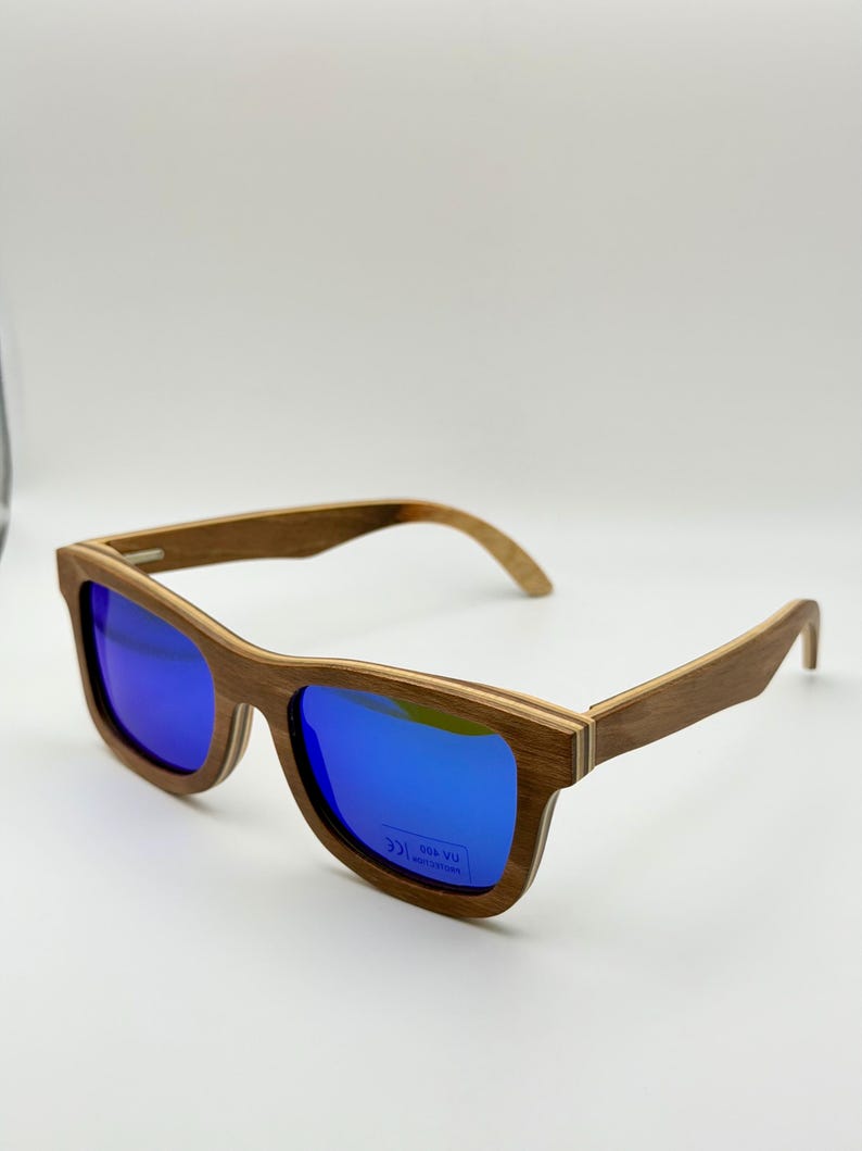 May include: Wooden-framed sunglasses with blue mirrored lenses. The sunglasses have a rectangular shape and a natural wood grain finish. The lenses reflect a bright blue color, and the frames are a light brown color.
