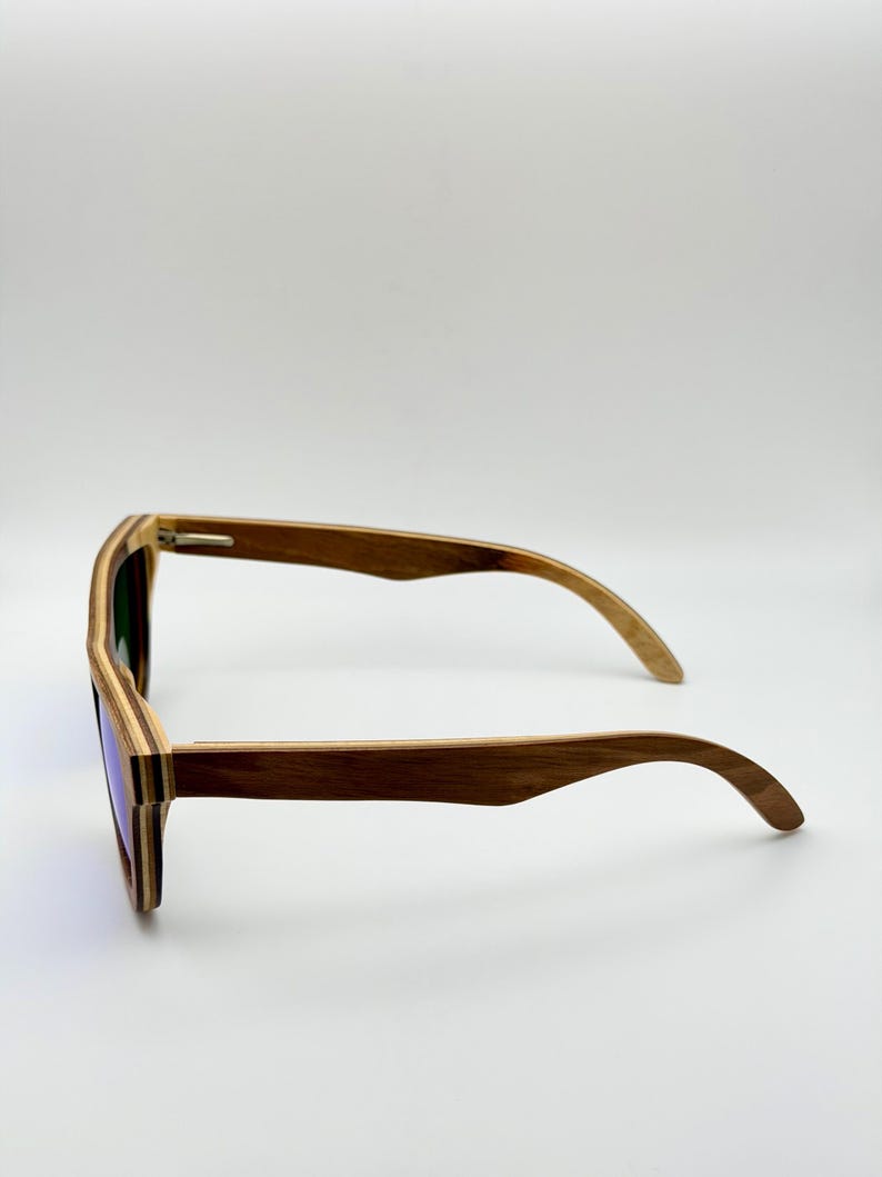 May include: Wooden sunglasses with a layered design. The frames are a mix of light and dark brown wood, and the lenses have a purple tint. The sunglasses are shown from a side profile.