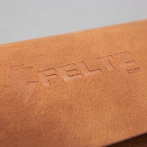 May include: Close-up of a brown leather item with the embossed word "FELTZ" and the word "GOOD". The leather has a textured surface and a warm, natural colour.