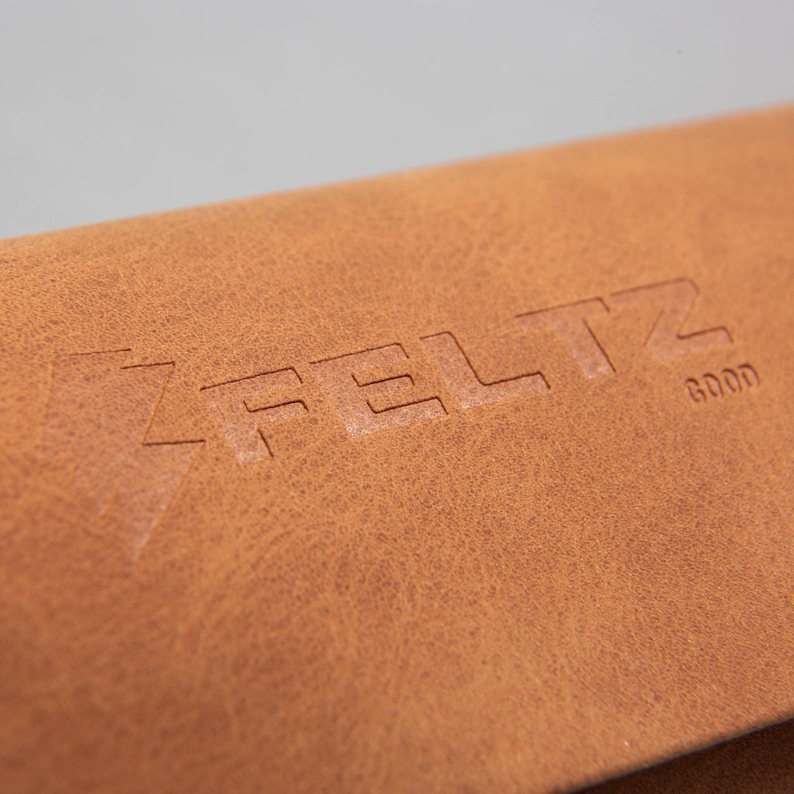 May include: Close-up of a brown leather item with the embossed word "FELTZ" and the word "GOOD". The leather has a textured surface and a warm, natural colour.