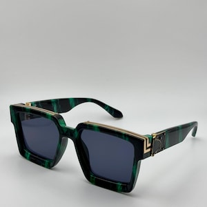 May include: Green and black square sunglasses with gold accents. The sunglasses have a unique, geometric design.