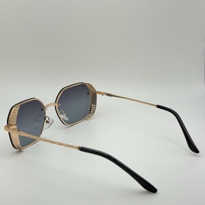 Pode incluir: &Oacute;culos de sol com arma&ccedil;&atilde;o dourada e design geom&eacute;trico. As lentes s&atilde;o cinza gradiente e as hastes s&atilde;o douradas com extremidades pretas. Os &oacute;culos de sol t&ecirc;m um visual moderno e elegante.