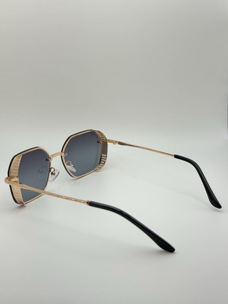 Pode incluir: &Oacute;culos de sol com arma&ccedil;&atilde;o dourada e design geom&eacute;trico. As lentes s&atilde;o cinza gradiente e as hastes s&atilde;o douradas com extremidades pretas. Os &oacute;culos de sol t&ecirc;m um visual moderno e elegante.