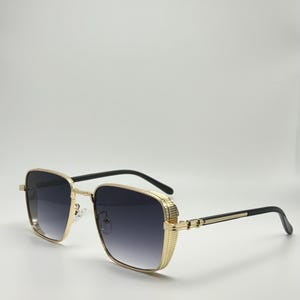 Peut inclure: Lunettes de soleil carr&eacute;es avec des montures dor&eacute;es et des verres noirs. Les lunettes ont une monture en m&eacute;tal dor&eacute; textur&eacute;e.