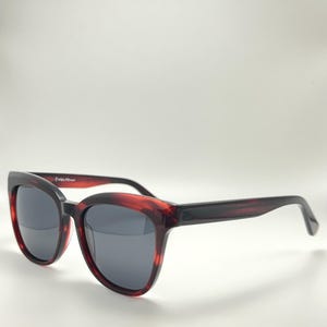 Puede incluir: Gafas de sol carey rojas y negras con lentes gris oscuro. Las gafas de sol tienen una montura gruesa y forma de ojo de gato. Las patillas son de color negro liso. La marca "FELTE" está impresa en la patilla izquierda.