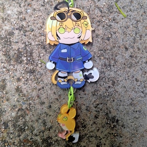May include: A green keychain with a cartoon character wearing a blue jumpsuit and goggles. The character is holding a small yellow mouse with green eyes.
