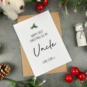 May include: A white card with a green holly sprig and red berries. The card reads "Happy First Christmas as my Uncle Love Esme x".