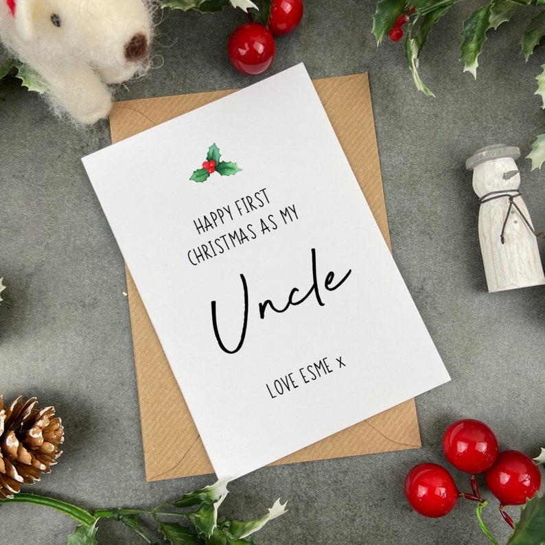 May include: A white card with a green holly sprig and red berries. The card reads "Happy First Christmas as my Uncle Love Esme x".