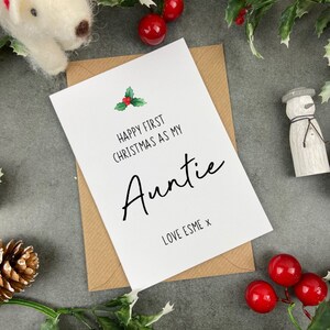 May include: A white card with a green holly sprig and red berries. The card reads "Happy First Christmas as my Auntie Love Esme x".