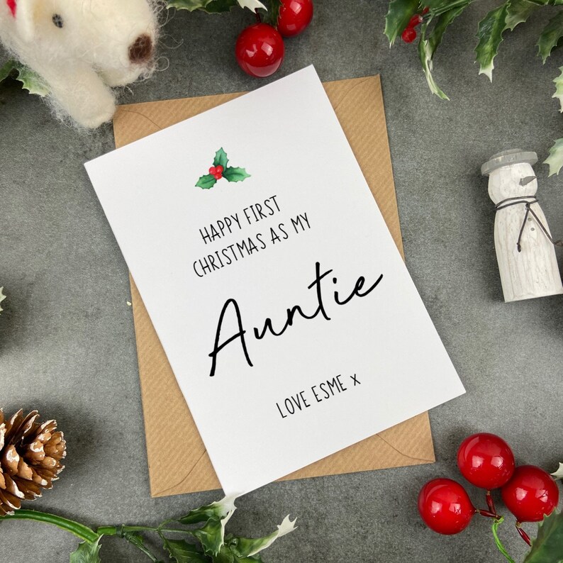 May include: A white card with a green holly sprig and red berries. The card reads "Happy First Christmas as my Auntie Love Esme x".