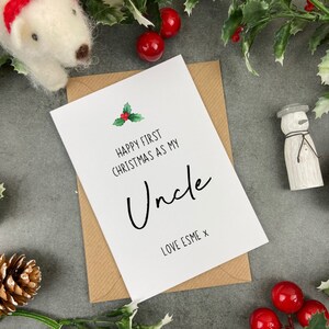 May include: A white card with a green holly sprig and red berries. The card reads "Happy First Christmas as my Uncle Love Esme x".