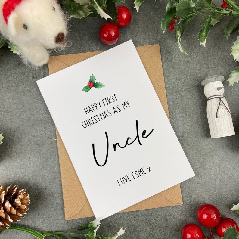May include: A white card with a green holly sprig and red berries. The card reads "Happy First Christmas as my Uncle Love Esme x".