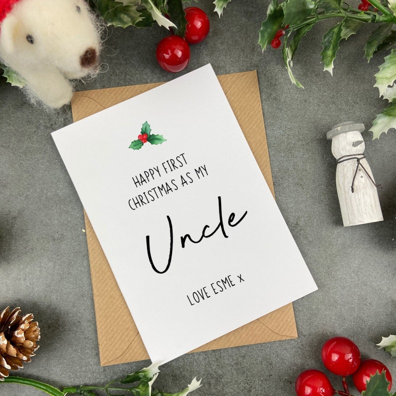May include: A white card with a green holly sprig and red berries. The card reads "Happy First Christmas as my Uncle" with the word "Uncle" in cursive. The card is signed "Love Esme x".