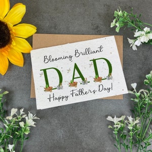 May include: A green card with the words "Blooming Brilliant Dad" and "Happy Father's Day!" in black text. The word "Dad" is decorated with small images of gardening tools and plants.