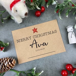 May include: A brown card with a red star and the text "Merry Christmas Ava Love From" on it. The card is surrounded by holly and a white polar bear.