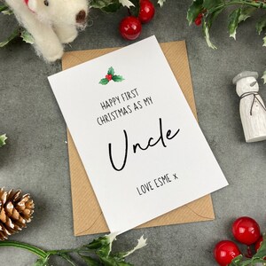 May include: A white card with a red and green holly sprig illustration. The card reads "Happy First Christmas as my Uncle Love Esme x".