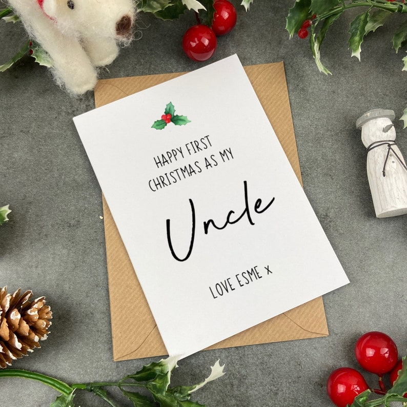 May include: A white card with a red and green holly sprig illustration. The card reads "Happy First Christmas as my Uncle Love Esme x".