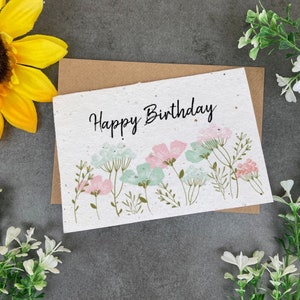 May include: A white card with the text "Happy Birthday" in black script. The card is decorated with a row of pink and blue flowers and green leaves.