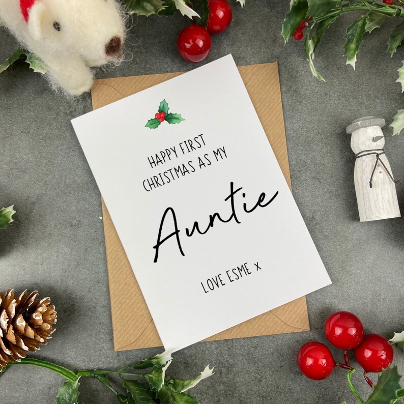 May include: A white card with a red and green holly sprig illustration. The card reads "Happy First Christmas as my Auntie Love Esme x".