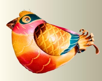 May include: A bird-shaped object crafted from multi-colored leather, featuring a vibrant gradient of red, orange, and yellow on the body. The wings display a textured, scale-like pattern in shades of brown and gold, accented by dark teal wing tips.