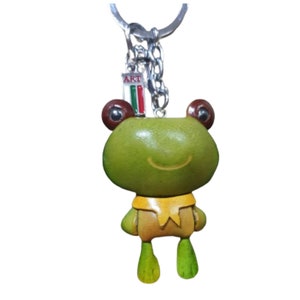 Könnte beinhalten: Grüner Leder-Fröschchen-Schlüsselanhänger mit gelbem Schal und braunen Augen. Der Schlüsselanhänger hat einen silbernen Ring und ein kleines Schild mit der Aufschrift "ART" und einer italienischen Flagge.