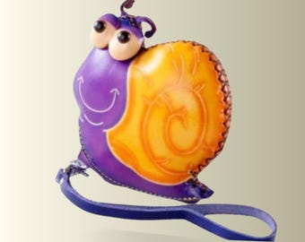 May include: A whimsical, handcrafted leather snail figurine. The snail features a purple body, a yellow shell with brown accents, and large, expressive eyes. A blue leather strap is attached. This decorative item is suitable for home decor.