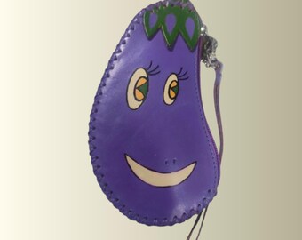 May include: A purple, eggplant-shaped coin purse with a smiling face design. The purse features a zipper closure, a small wrist strap, and green and white accents. The edges are stitched with a contrasting thread.