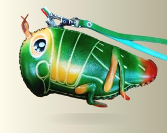 May include: A grasshopper-shaped leather pouch featuring a vibrant green body with yellow and orange accents, large black and white eyes, and a small antenna. A silver metal clasp is attached to a green strap for hanging or carrying purposes.