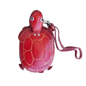 Könnte beinhalten: Rote Leder-Turtleschlüsselbundbörse mit einem Riemen. Die Börse hat ein genähtes Design und zwei schwarze Augen.