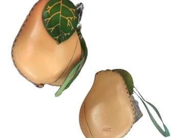 May include: Two tan leather pear-shaped purses with green leather leaves and straps. The purse on the left has a green leaf with yellow veins. The purse on the right has the word "ART" stamped on the front.