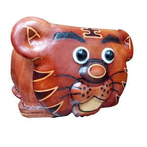 May include: A brown leather coin purse shaped like a tiger head with black painted stripes, white and black plastic eyes, a dark brown nose, and black whiskers. The leather features embossed details and visible stitching along the bottom edge.