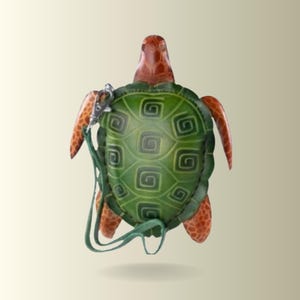 Könnte beinhalten: Eine schildkrötenförmige Tasche mit einem grünen Panzer mit Spiralmuster sowie orange-braunen Gliedmaßen und Kopf. Die Tasche verfügt über einen grünen Riemen, der mit einem silberfarbenen Metallkarabiner befestigt ist und die Form einer Schildkröte zeigt.