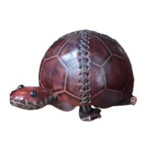 May include: A brown leather turtle figurine with a stitched shell. The turtle has a detailed head and legs.