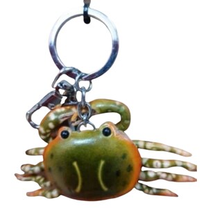 May include: A green and orange crab keychain with a silver key ring. The crab has a detailed design with realistic features.