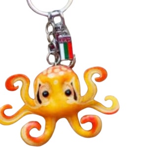 May include: A yellow octopus keychain with red accents and white spots. The keychain has a metal ring and a small charm with the flag of the United Arab Emirates.