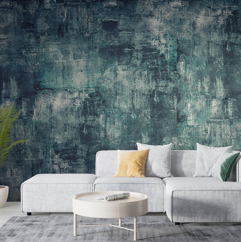 K&ouml;nnte beinhalten: Ein modernes Wohnzimmer mit einer strukturierten Wand mit abstrakter Kunst in T&uuml;rkis und Grau. Ein wei&szlig;es Ecksofa mit Kissen in Gelb, Wei&szlig; und Gr&uuml;n steht auf einem grauen Teppich. Ein runder, wei&szlig;er Couchtisch mit einer gerollten Zeitschrift.
