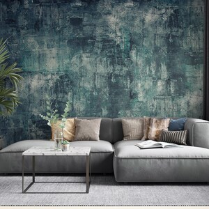 K&ouml;nnte beinhalten: Ein modernes Wohnzimmer mit einem grauen Ecksofa, dekorativen Kissen und einem Couchtisch mit Marmorplatte. Die Wand ist mit einem strukturierten t&uuml;rkis-grauen Wandbild geschm&uuml;ckt. Eine Topfpflanze und eine Vase mit Gr&uuml;npflanzen.