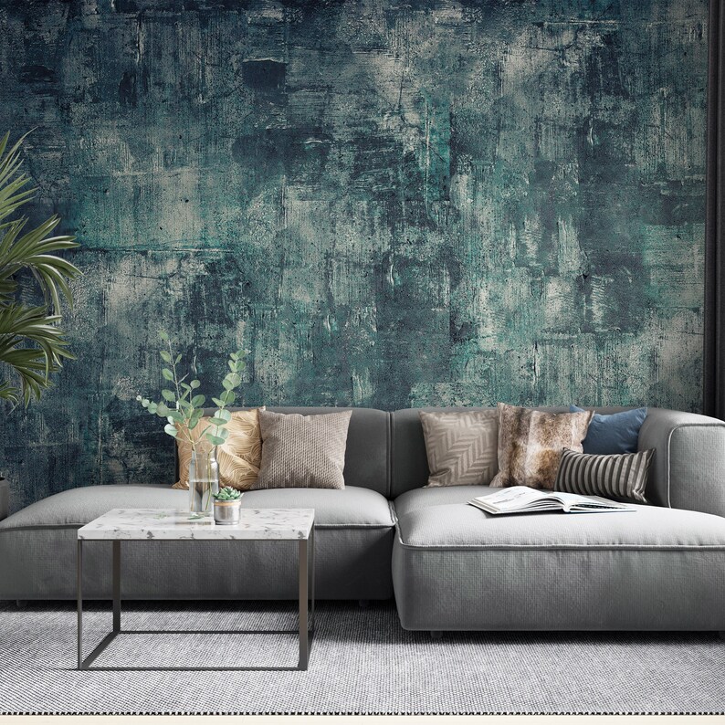 K&ouml;nnte beinhalten: Ein modernes Wohnzimmer mit einem grauen Ecksofa, dekorativen Kissen und einem Couchtisch mit Marmorplatte. Die Wand ist mit einem strukturierten t&uuml;rkis-grauen Wandbild geschm&uuml;ckt. Eine Topfpflanze und eine Vase mit Gr&uuml;npflanzen.