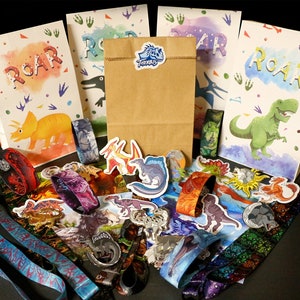 Könnte beinhalten: Eine Sammlung von Partyartikeln zum Thema Dinosaurier, darunter Papiertüten mit dem Text "ROAR" und Dinosaurierillustrationen, Aufkleber, Schlüsselbänder und Armbänder. Die Farbpalette umfasst Orange, Grün, Blau und Lila.