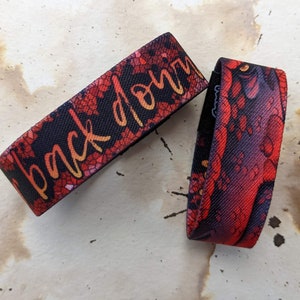 May include: Two red and black patterned wristbands. One wristband has the text "back down" in yellow lettering.