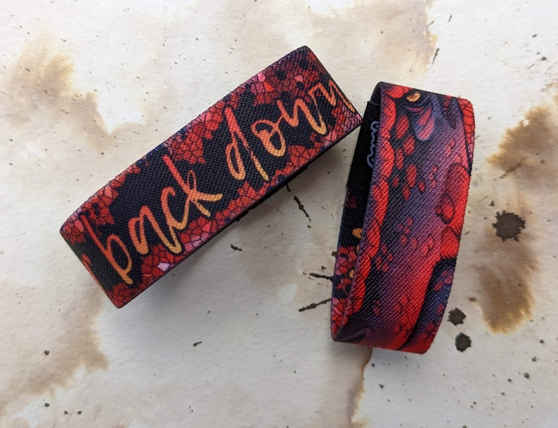 May include: Two red and black patterned wristbands. One wristband has the text "back down" in yellow lettering.