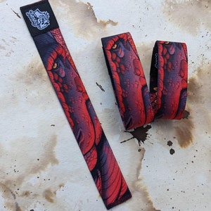 May include: Two red and black wristbands with a dragon design. The wristbands are made of woven fabric and have a black and white logo on one of the wristbands.