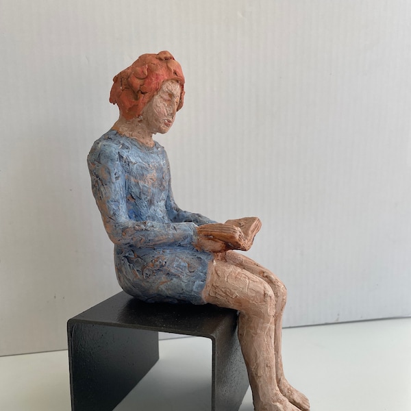 Sculpture en céramique peinte d'une femme assise lisant un livre