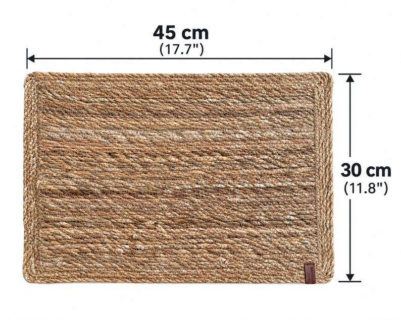 K&ouml;nnte beinhalten: Ein rechteckiges, geflochtenes Platzset aus naturfarbenen Fasern mit einem geflochtenen Rand. Das Platzset misst 45 cm in der Breite und 30 cm in der H&ouml;he. Eine kleine braune, rechteckige Lasche ist an der unteren rechten Ecke angebracht.