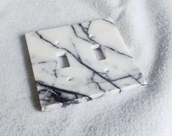 May include: A white marble light switch cover with black veining. The cover has two toggle switches.