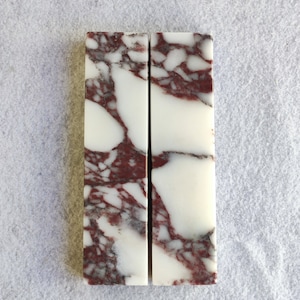 Op de afbeelding: Twee rechthoekige marmeren platen met een witte achtergrond en rode aderen. De marmer is gepolijst en glad.