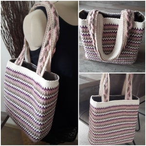 Puede incluir: Un bolso tote tejido a ganchillo con un patrón de rayas en tonos de blanco, rosa, morado y marrón. El bolso tiene asas trenzadas y un ribete blanco liso. El interior del bolso es de tela marrón oscuro.