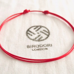 May include: A red string bracelet with a simple knot design. The bracelet is made of a thin, durable cord and is tied with a secure knot.