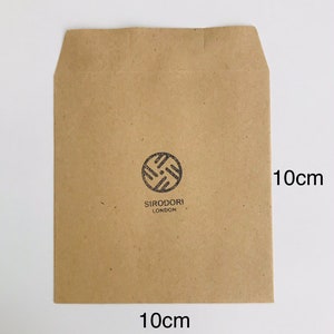 May include: A brown paper envelope, 10cm x 10cm, with a circular logo and the text "SIRODORI LONDON" printed in black. The envelope is rectangular with a folded top flap.